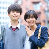 Smiling young man and woman with backpacks posing outdoors in front of a cityscape.