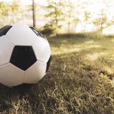 Close-up of a black-and-white soccer ball resting on sunlit grass with a blurred background.